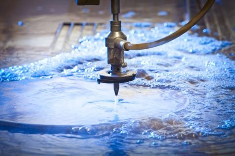 Waterjet cutting nozzle  close-up from metalwork industry. CNC waterjet machine at work cutting a steel plate.