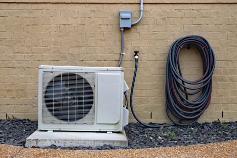Air-Conditioner-mini-split-system-next-to-home-with-painted-brick-wall-and-space-for-text-copy