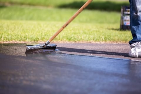 Close-up-of-a-home-owner-seal-coating-their-own-driveway.-They-are-using-the-broom-to-spread-out-the-sealer-on-the-driveway.