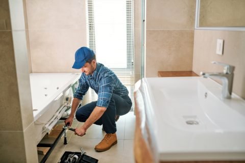 Young worker in uniform sitting on squats while fixing or fastening detail Bathroom Remodeling Service in Augusta, GA