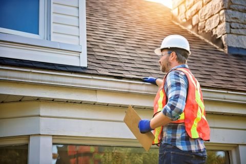 man with hard hat standing on steps inspecting house roof Roof Inspection Cary, NC