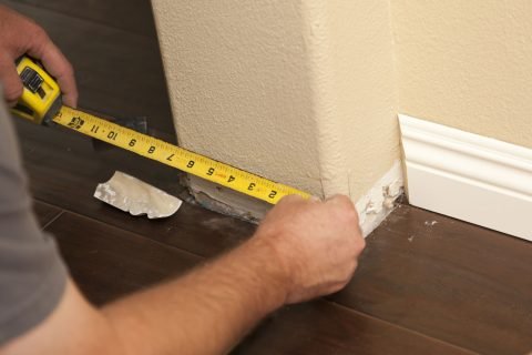 Worker-measuring-the-side-of-the-wall-for-baseboard Worker-measuring-the-side-of-the-wall-for-baseboard