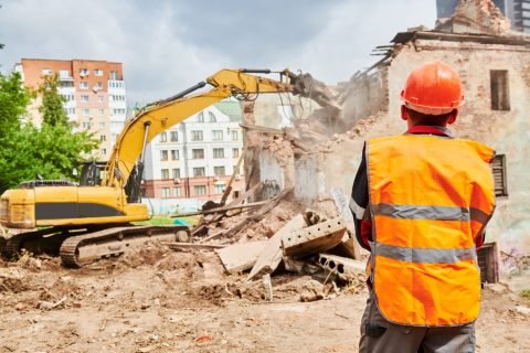 excavator loader crushing machine at secondary demolition or destroying works on construction site. Construction worker foreman is watching